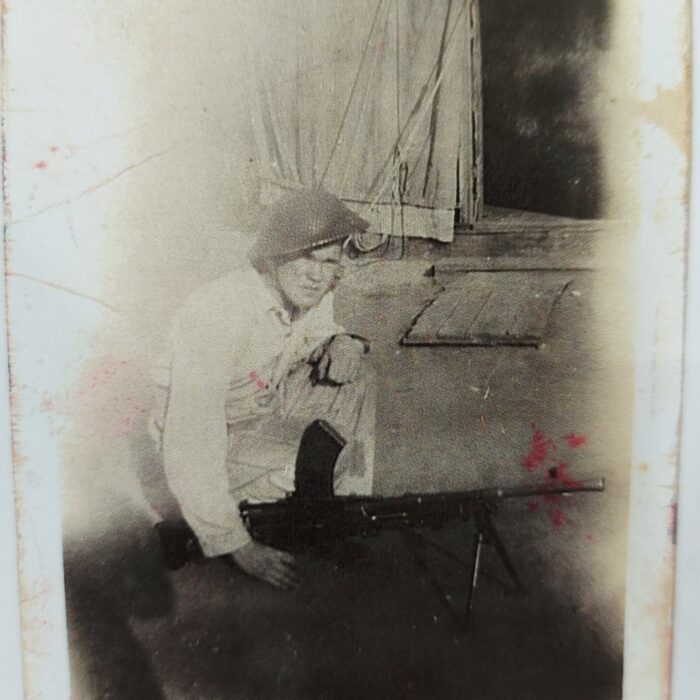 Private John V. Sinclair, c1942-1945, Mae Gulewich Black and white photo of a man crouching beside a building. He is in military uniform