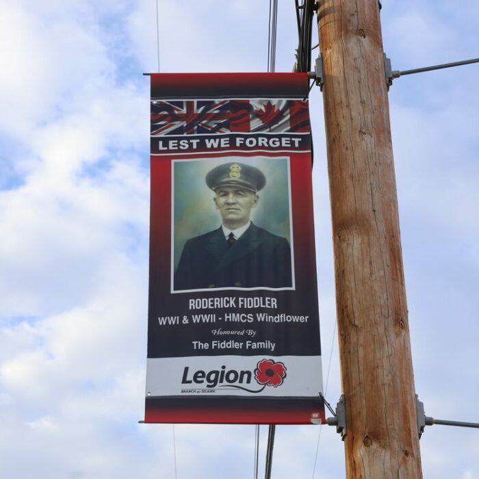 Colour photo of a banner hanging from the side of a telephone pole. The banner has a photo of Roderick Fiddler on it