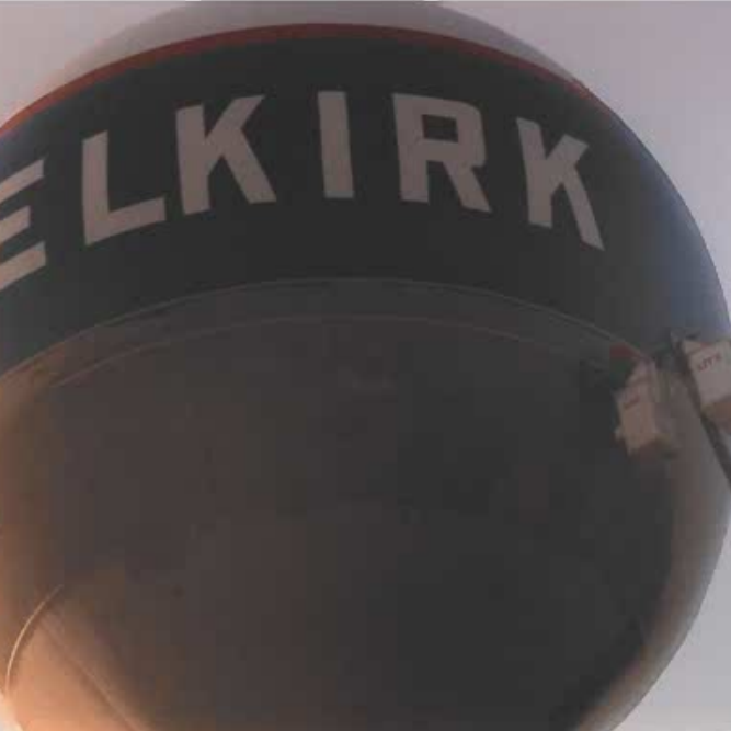 Colour photo of the Selkirk Water tower reservoir. The bowl is white with a blue band trimmed in red. The letters read 'selkirk' and are white