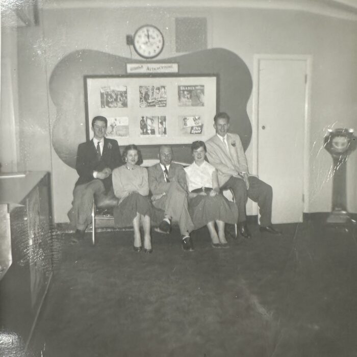 A black and white photo of a group of young people sitting in front of a photo display and a clock