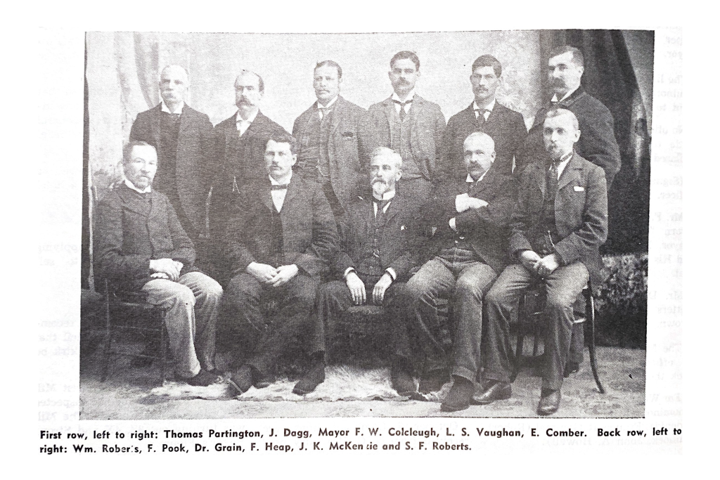 Grainy black and white image of town council. Eleven men are seated