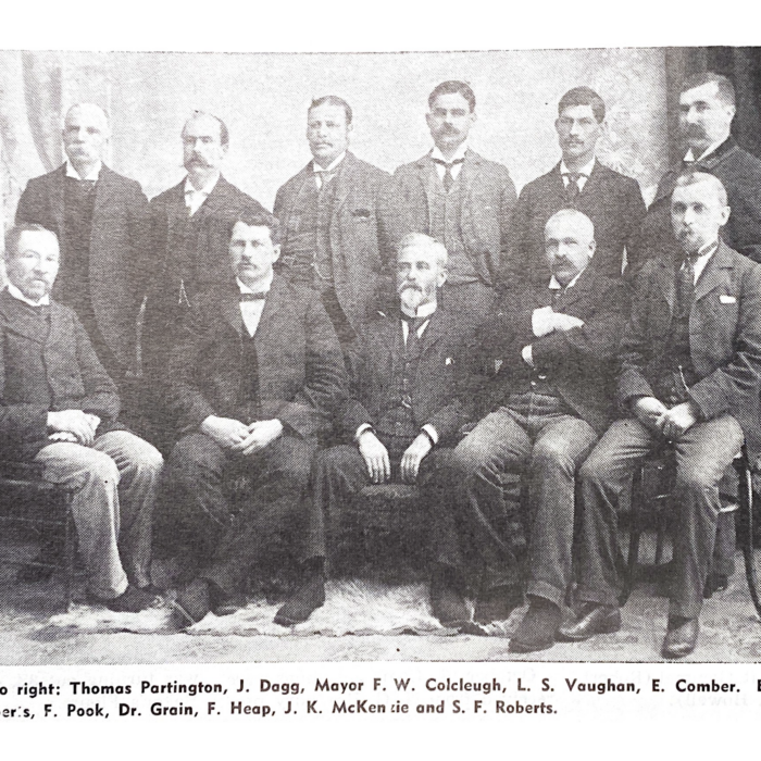 Grainy black and white image of town council. Eleven men are seated