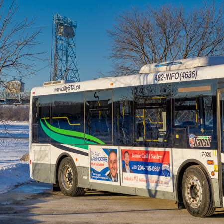 Colour image of a transit bus parked in a parking lot. The blue bridge can be seen in the background