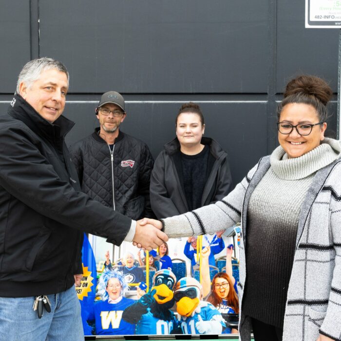 Colour image of four people at a bus stop. A man and a woman shake hands in front of a bench