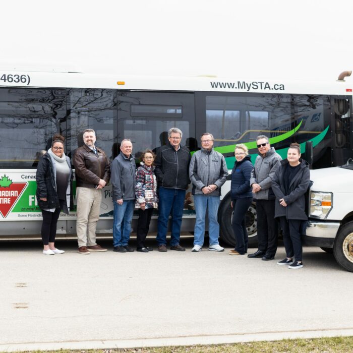 A colour photo of a group of people standing in front of a bus