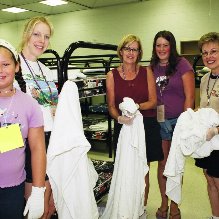 Group of women inside sleeping quarters holding sheets