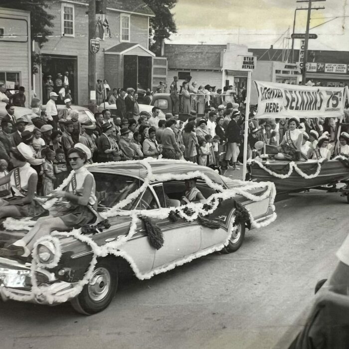 Women Sitting on Car, 1957, Selkirk Museum Collection black and white photo of two women sitting on a car hood in the parade