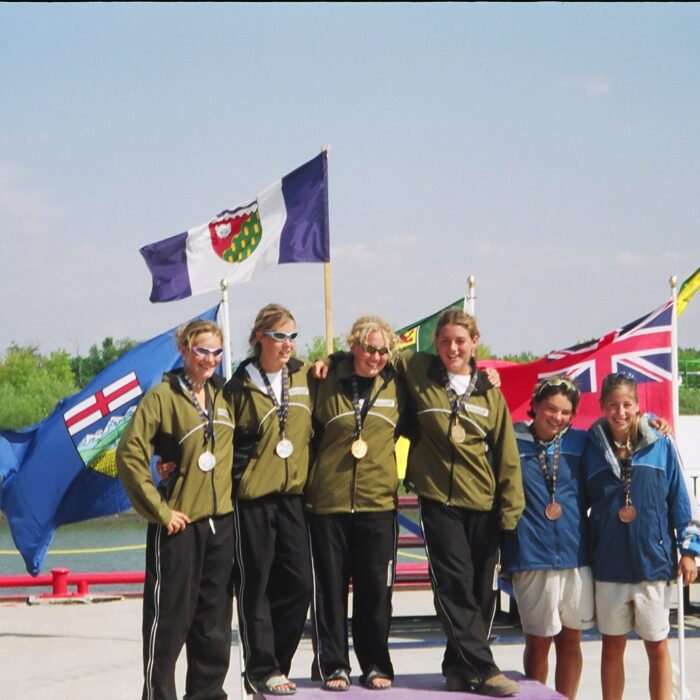 Group of athletes standing on podium wearing medals. Flags are in the background