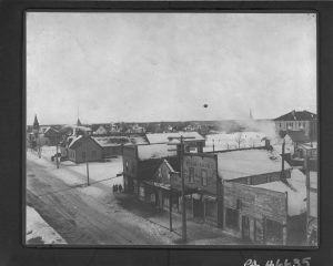 This is a black and white photo taken in the winter of 1910 overlooking West Selkirk Manitoba Circa. There are buildings down the street, and group of houses in the background.