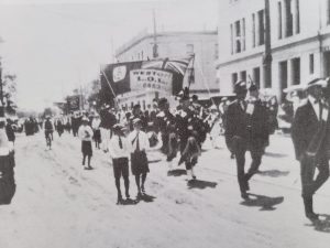 This is a black and white photo taken in 1919 of the Peace Parade. There are people marching down the streets holding banners.