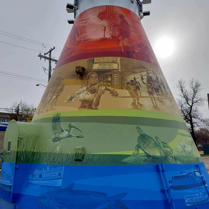 Colour image of a mural painted on the base of the Selkirk Water Tower. There are four colours used, red, orange green, and blue. Each band of colour has various scenes of people, places, and animals