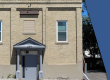 Photo shows the front of the Eaton Masonic Hall. The front door overhang supported by two pillars. Two windows on either side of the building