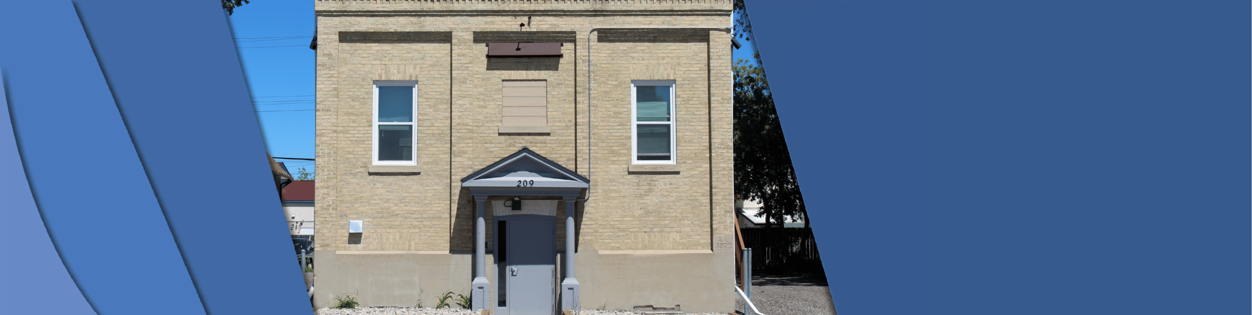 Photo shows the front of the Eaton Masonic Hall. The front door overhang supported by two pillars. Two windows on either side of the building