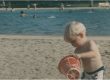 Photo shows a young child playing in the sand with a bucket at the poolside