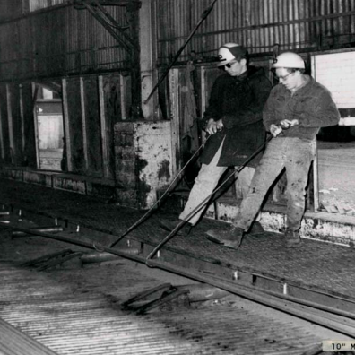 Cooling Bed Manually Moving Bars, Date Unknown, Gerdau Two people moving bars inside the Manitoba Rolling Mills