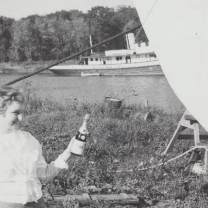 Sharon Purvis Performing the Official Launch of the Joe Simpson After Upgrades, 1967, Fraser Stewart A woman holding a bottle of champagne in front of the Joe Simpson boat