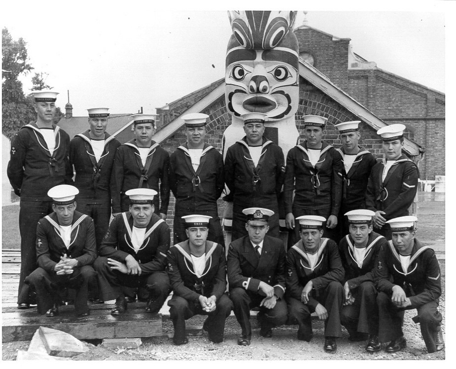 Fifteen men in uniform posing in front of the Hosagami totem pole
