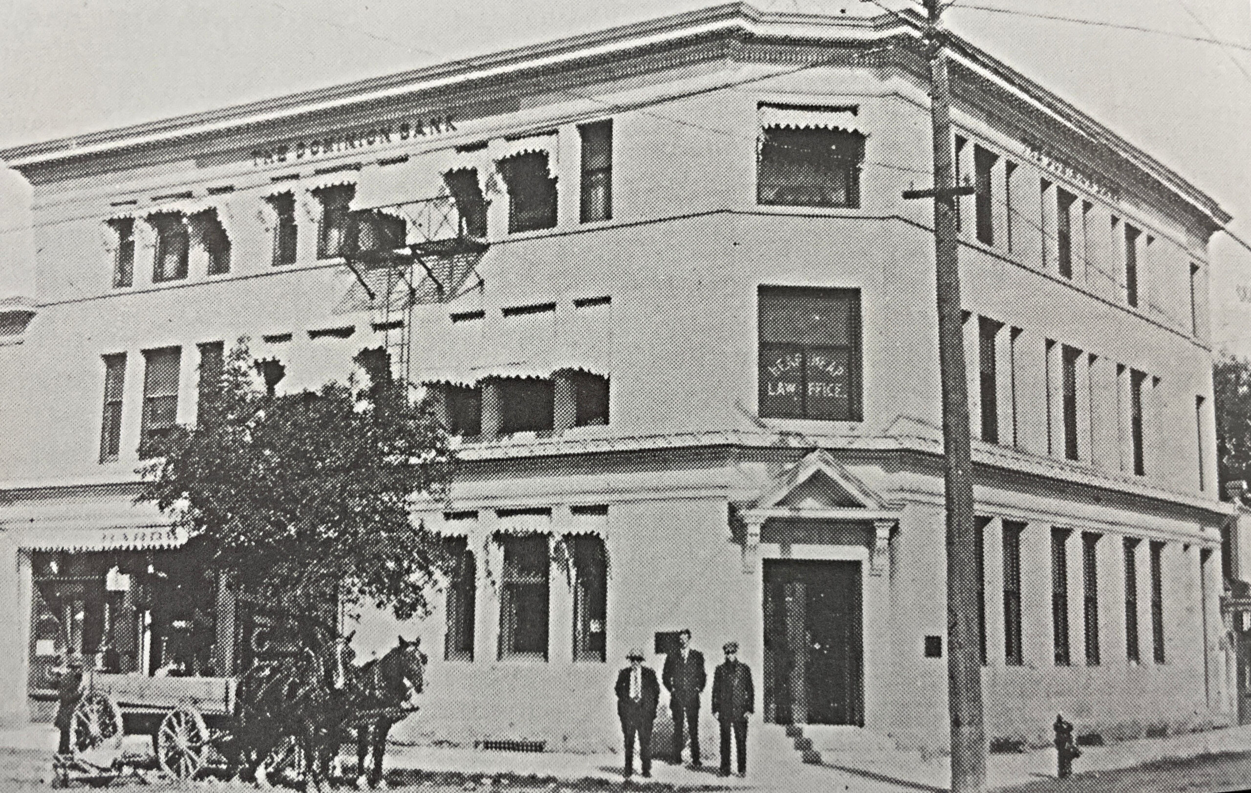 Black and white photo of the Dominion Bank, with 3 men in suits standing in front of the building