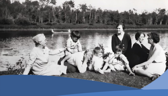 A image of eight people sitting on the banks of a river in Clandeboye Manitoba.. there are four adult women, one adult man, and three young children.