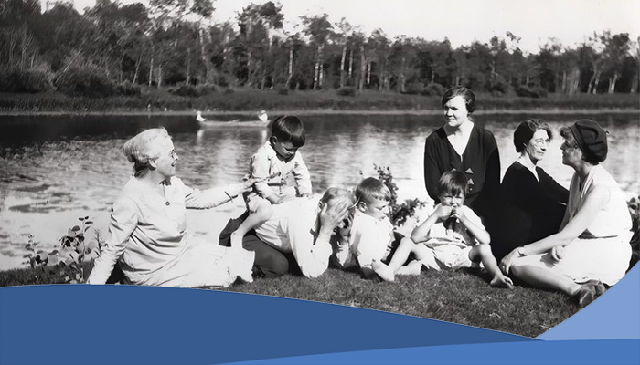 A image of eight people sitting on the banks of a river in Clandeboye Manitoba.. there are four adult women, one adult man, and three young children.