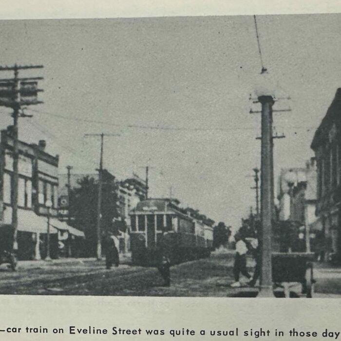 Electric Car train on Eveline street in Selkirk MB. There are buildings in the background and there are people on the sidewalk