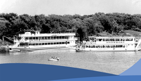 The Paddlewheel Queen and the Paddlewheel Princess in the water with a forest in the background