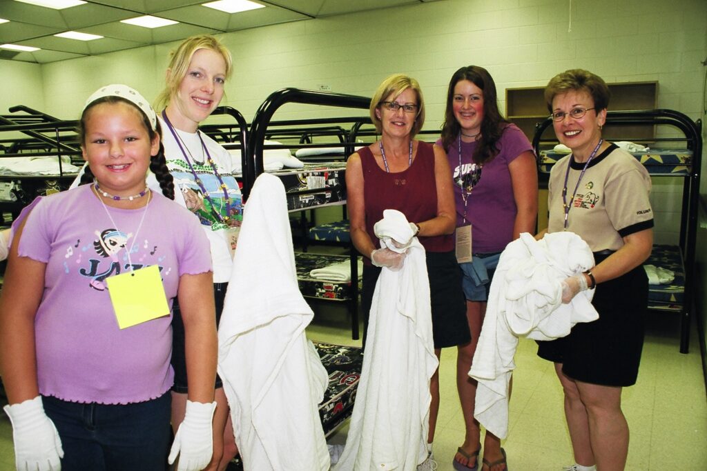 People smiling at the camera holding towels with bunk beds in the background