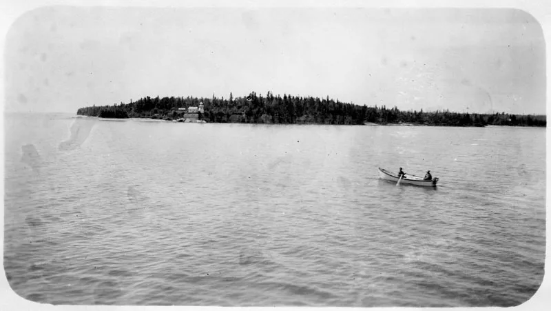 Two people canoeing on lake, with lighthouse in background.