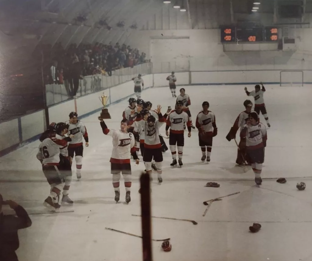 Coloured photo of the hockey team on the ice, holding up a gold championship cup.