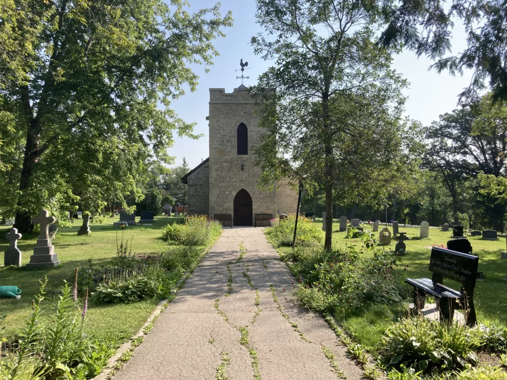 Photo of stone church surrounded by trees and headstones.