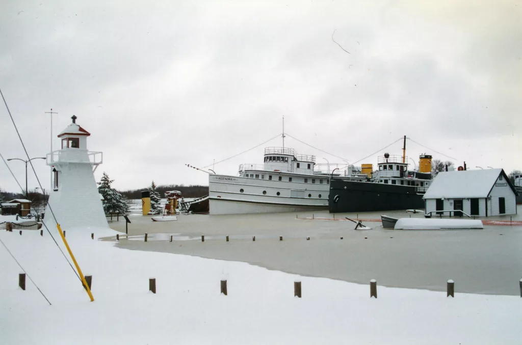 Colour image of lighthouse near boats, all covered in snow.