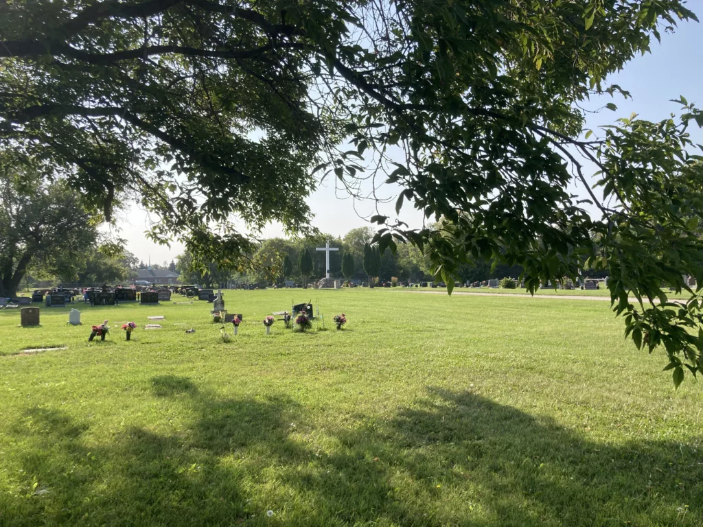Photo of field with headstones and a white cross.