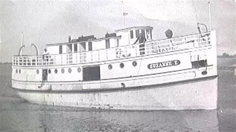 Vertical black and white photo of a boat sailing in water.