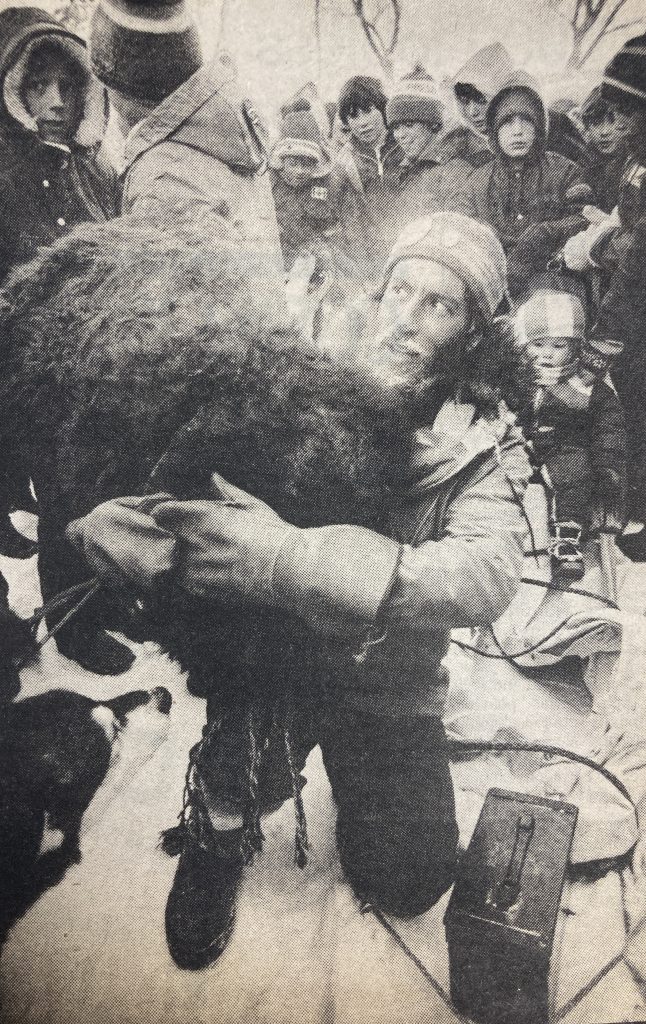 Man shown carrying a large bundle of fur with a crowd of children shown the in background