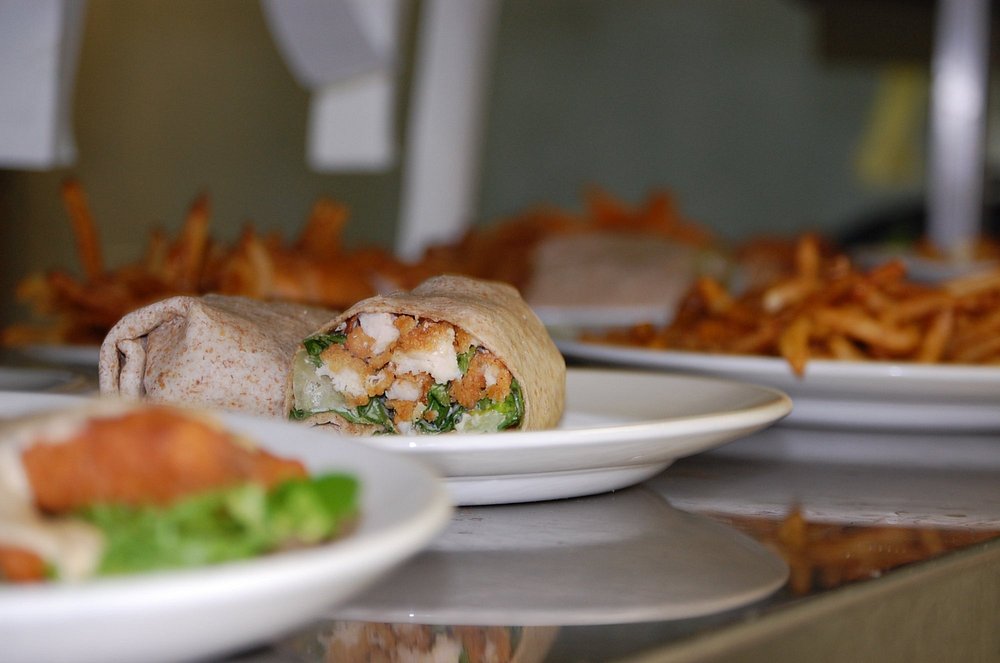 Colour photo of plates of food, including a wrap and french fries.