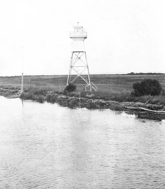 Vertical photo of a lighthouse at the edge of a river.