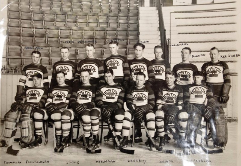 Black and white image of the Boston Bruins posing for a group photo in front of bleachers