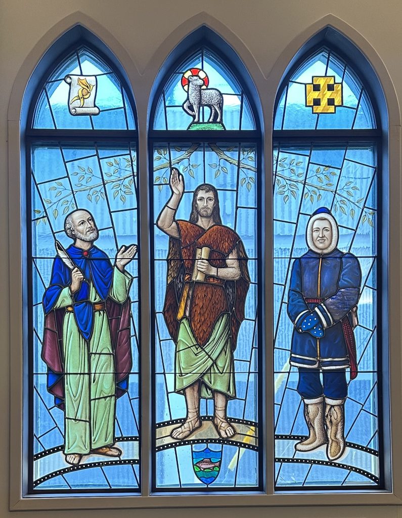 Large three panel window shows three figures. Above each figure is an arch containing a symbol