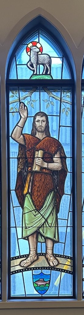 John the Baptist stands with his hand in the air and the other holding a scroll