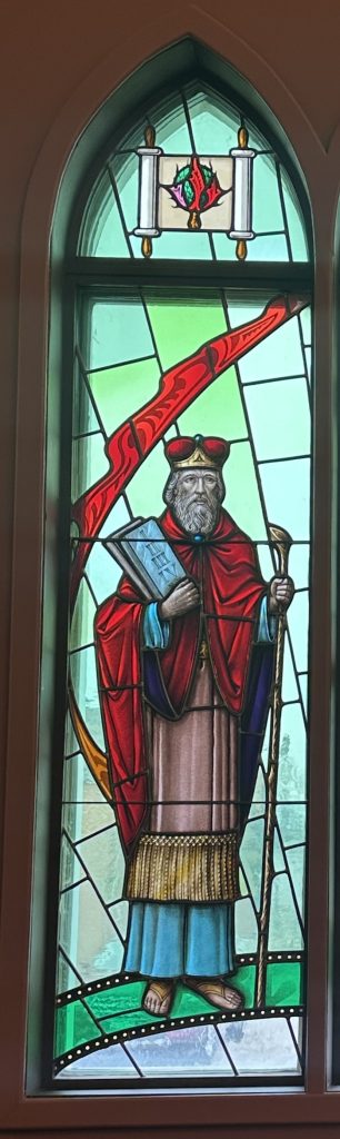 Moses is shown wearing red robes, holding a rod, and the ten commandments. He is against a green background