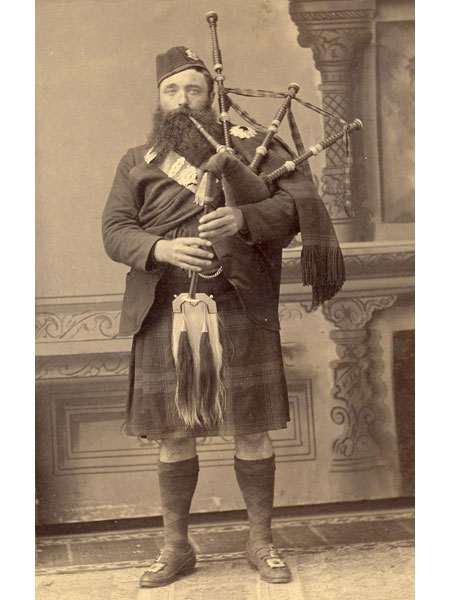 Image of a man wearing a kilt, sporan, and holding bagpipes