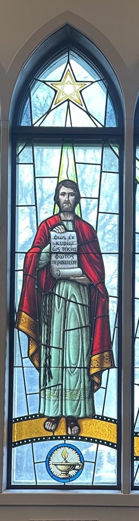 Man with red robe stands holding a scroll