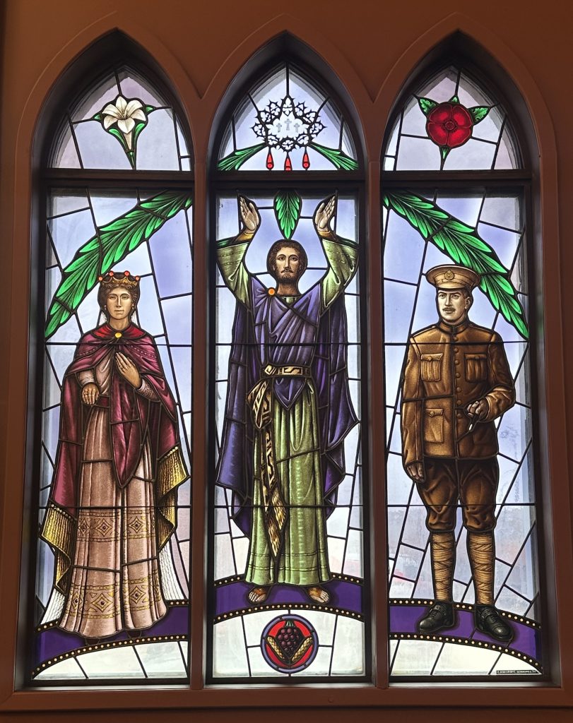 Large three panel window shows three figures. Above each figure is an arch containing a symbol