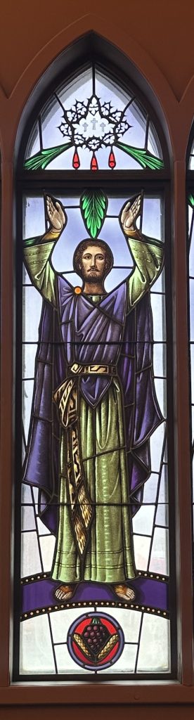 Stephen stands with his arms up above his head. He is wearing a green and purple robe