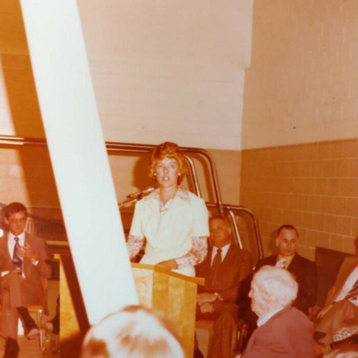 Bev Stewart at Selkirk Community Pool Opening, 1975, Kinsmen Scrapbook Selkirk Musuem Collection Brown image of Bev Stewart speaking at a podium
