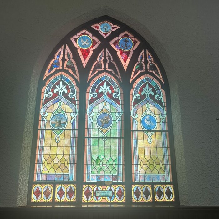 Stained glass window with red, blue, yellow, and green. Three panels worked into one