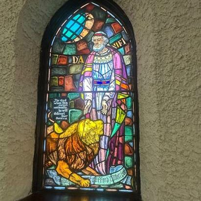 Stained glass window with Daniel wearing a purple robe standing in front of a lion