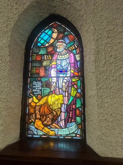 Stained glass window with Daniel wearing a purple robe standing in front of a lion