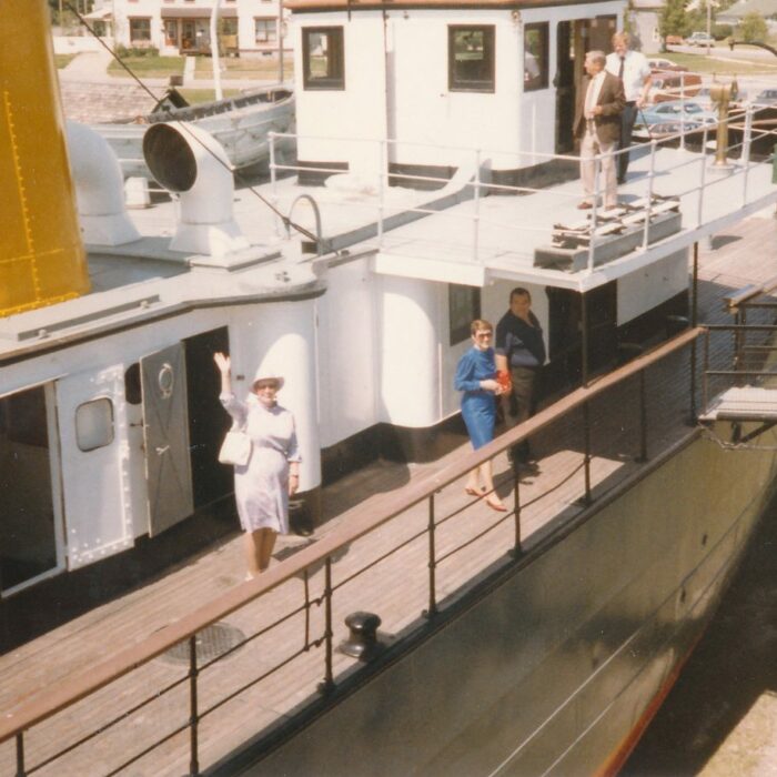 Aboard the Bradbury, July 1985, Fraser Stewart Colour photograph of the Bradbury. A woman dressed in a white skirt suit and a hat waves at the camera