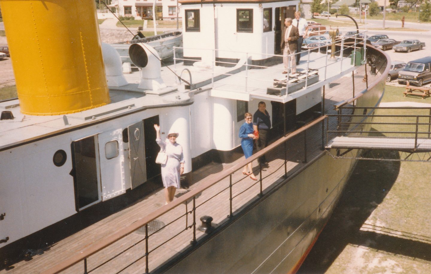 Colour photograph of the Bradbury. A woman dressed in a white skirt suit and a hat waves at the camera